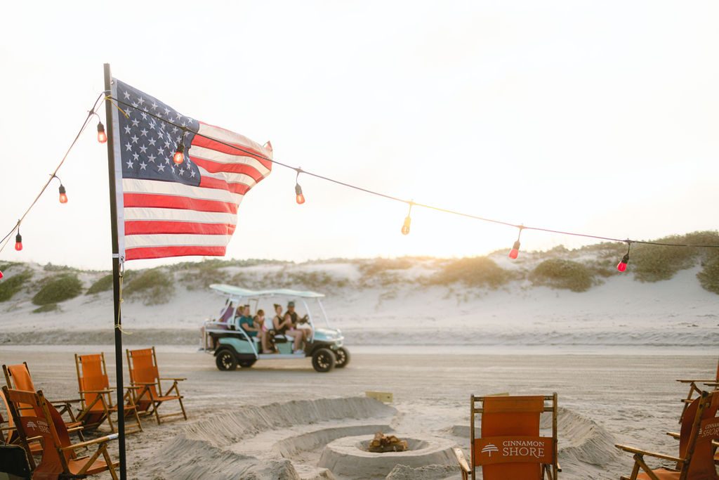 American flag waving over Cinnamon Shore beach chairs and a sand fire pit with string lights at sunset during the Memorial Day flag ceremony in Port Aransas, Texas