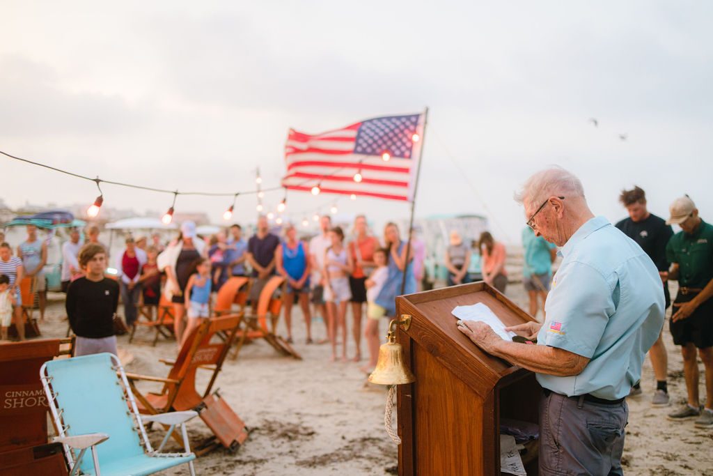 Elderly veteran reading a speech at a podium while the community listens during the Cinnamon Shore Memorial Day beach ceremony in Port Aransas, Texas