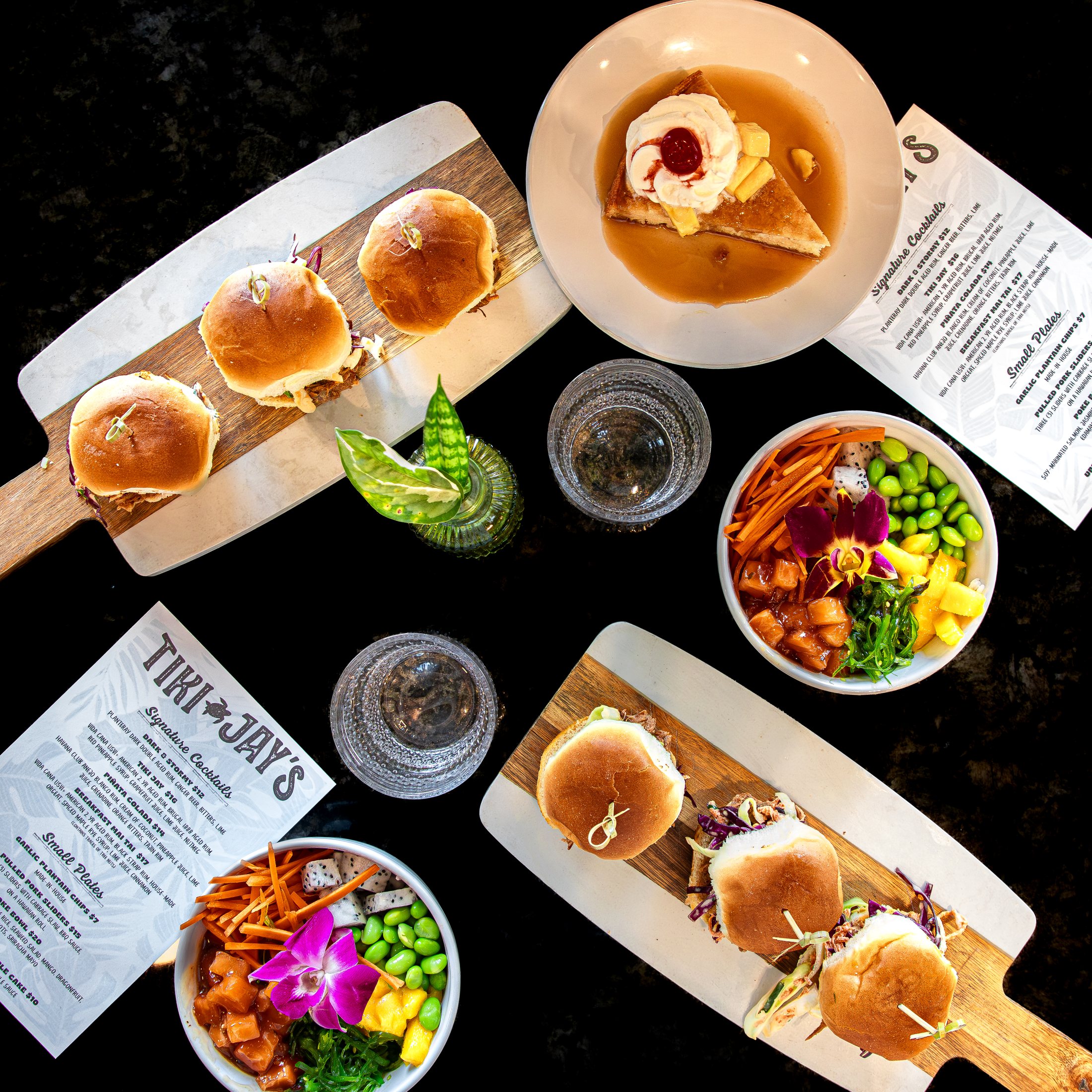 Tiki Jay's spread featuring a colorful poke bowl, sliders, small plates, and coastal drinks