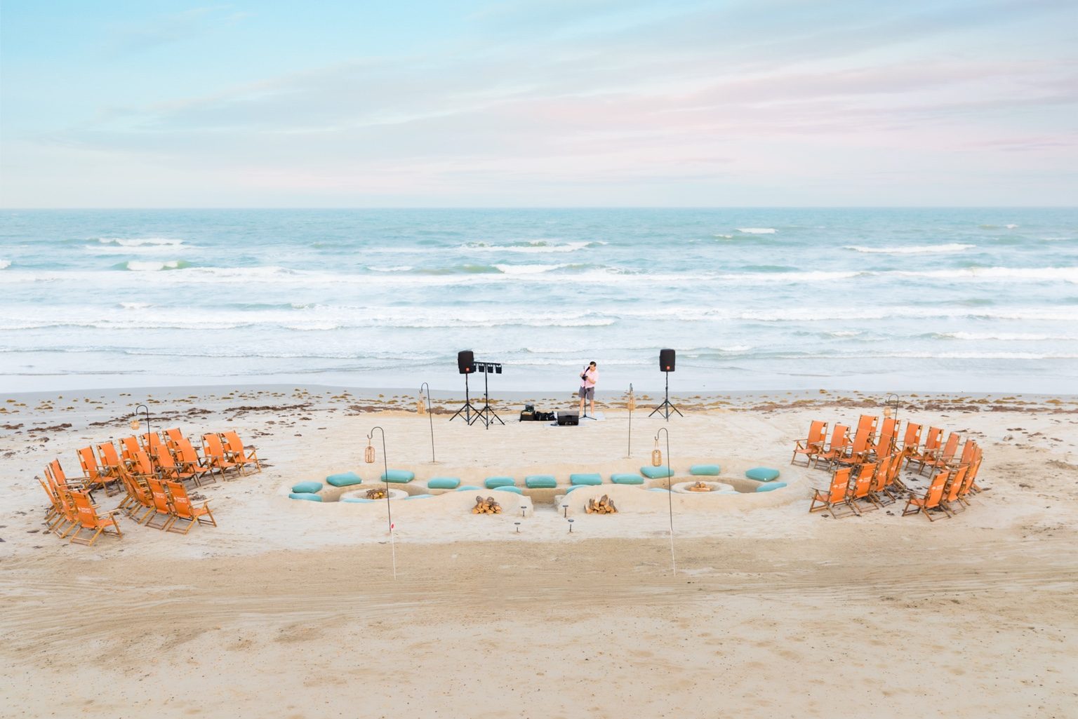 Twin beach bonfire seating areas with orange chairs, turquoise cushions, lanterns, and live music beside the Gulf at Cinnamon Shore.