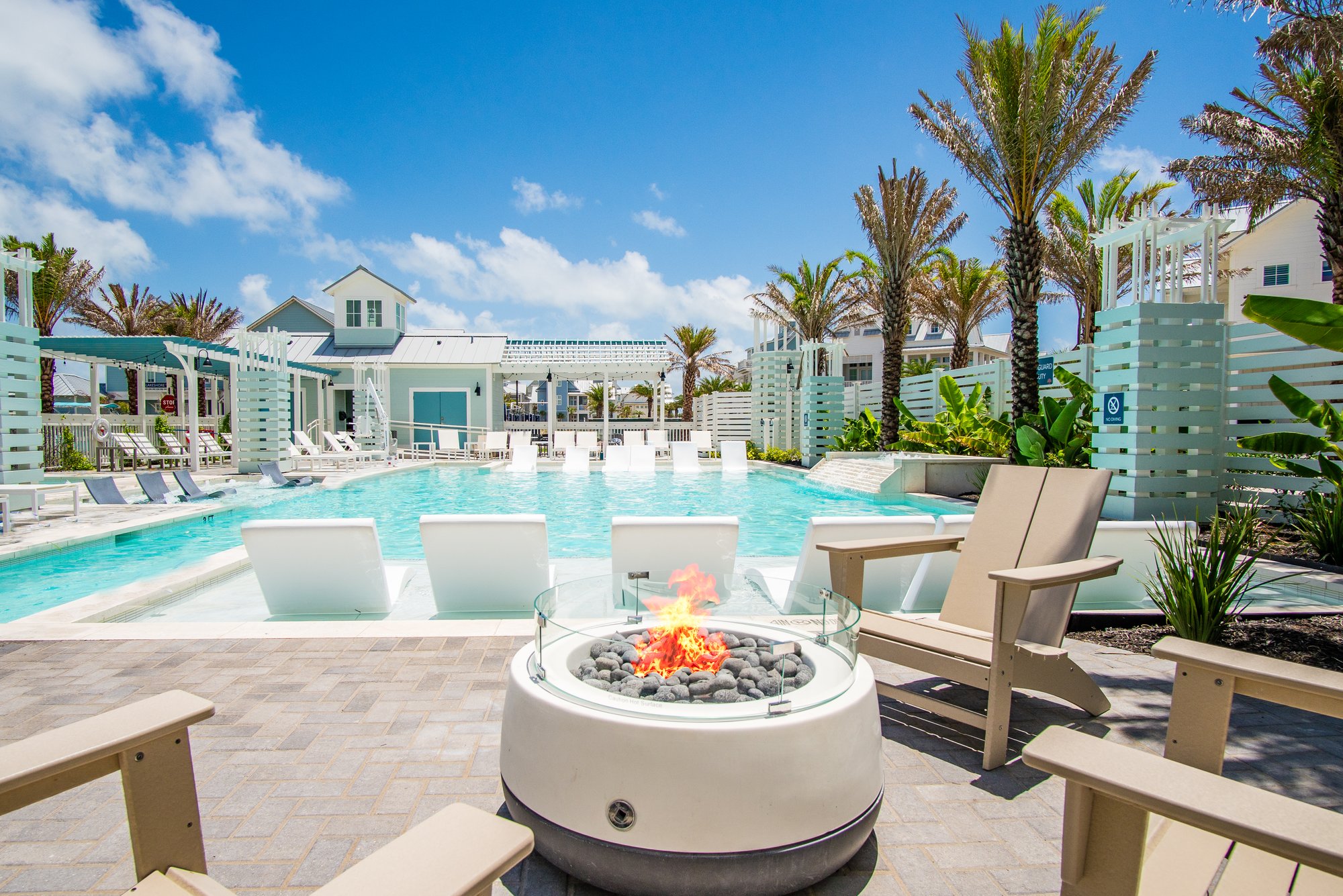 Neighborly Square Pool at Cinnamon Shore South with palm trees, fire pit seating, and coastal homes
