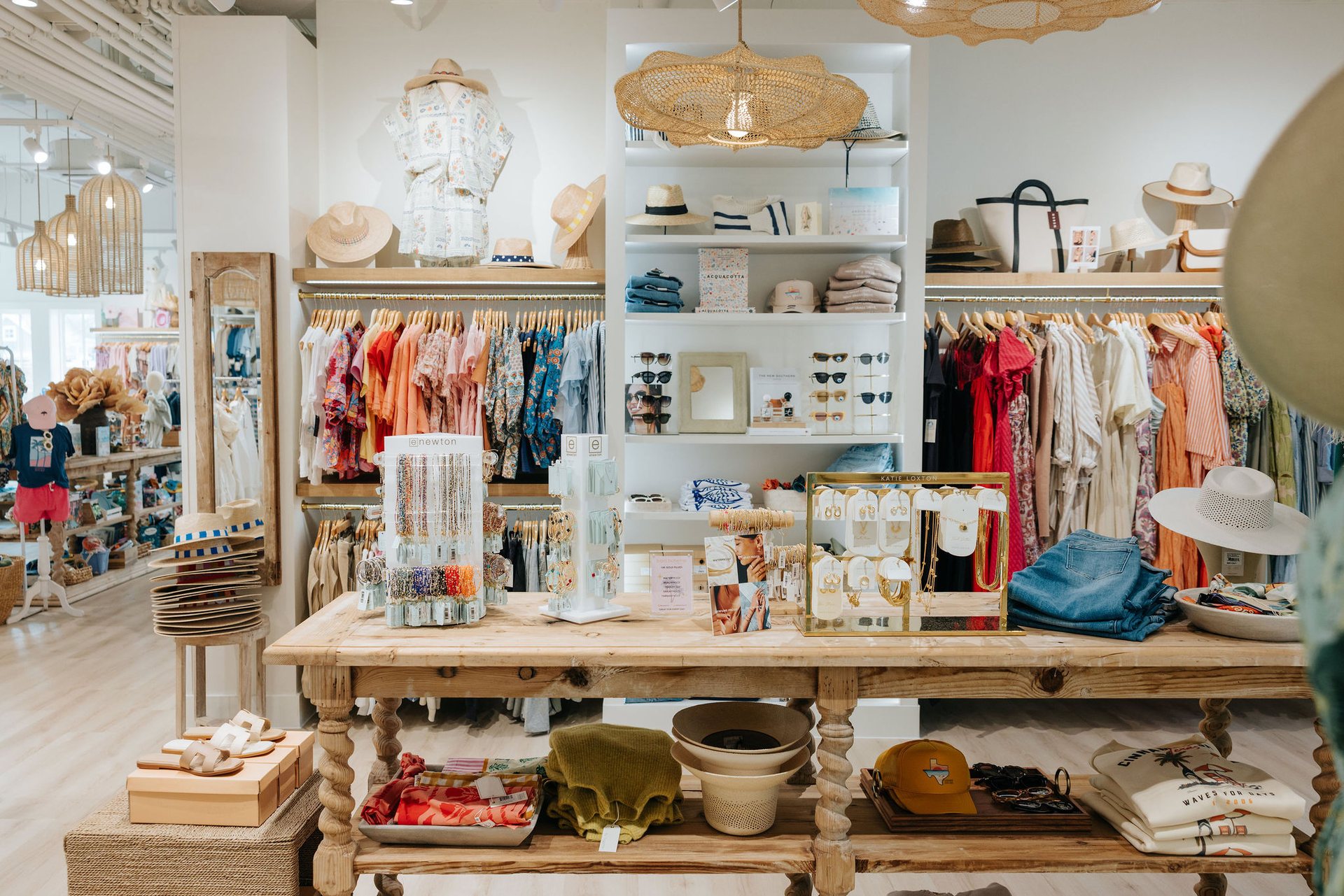 Resort wear, jewelry, hats, denim, and gifts arranged on a wooden table at The Boutiques at Cinnamon Shore