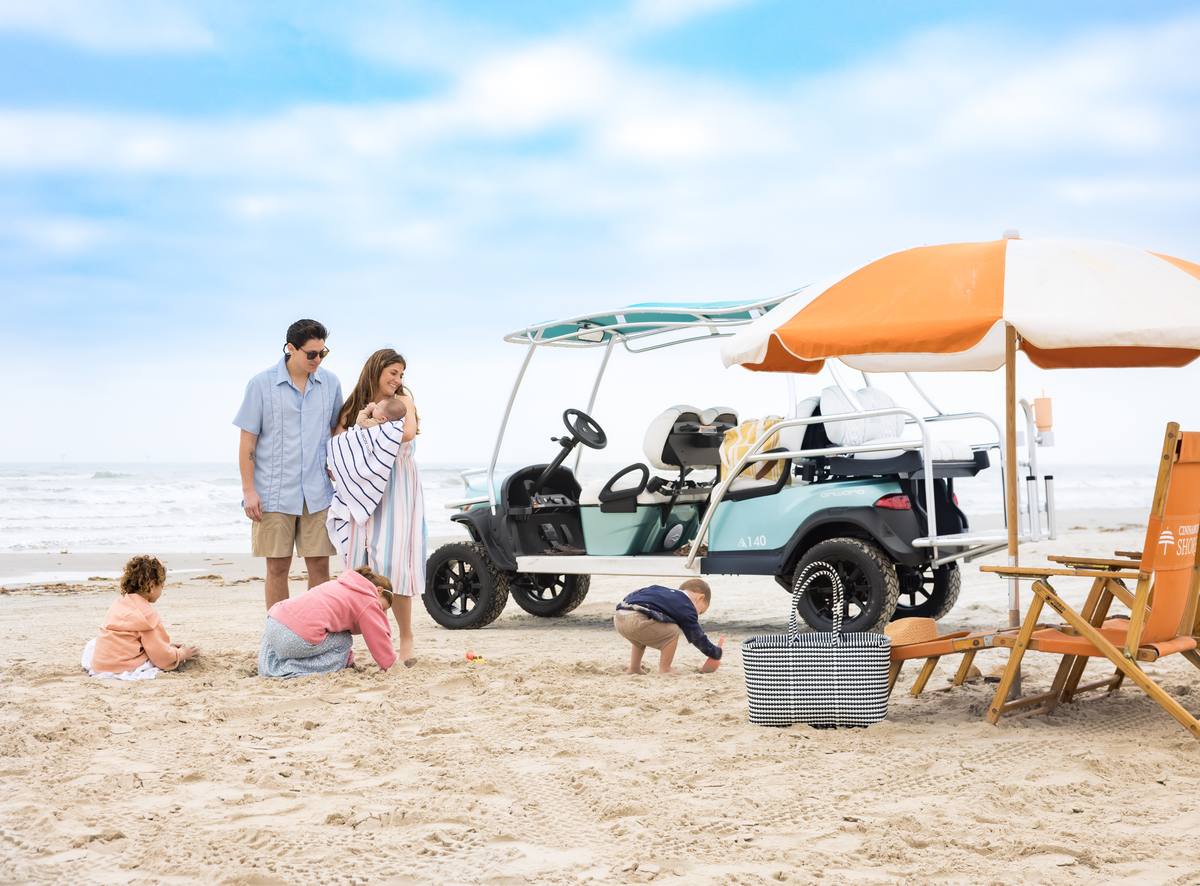 A family enjoys a beach day with their six-seater golf cart, umbrella, and beach chairs on the sand at Cinnamon Shore.