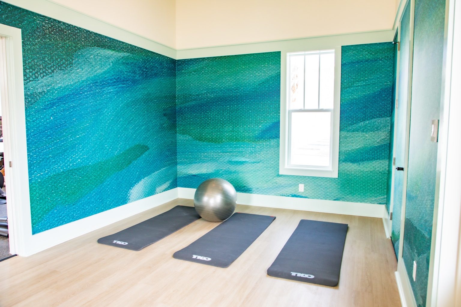 Sea Glass Fitness Center stretch room with yoga mats, exercise ball, and teal coastal wall mural at Cinnamon Shore.