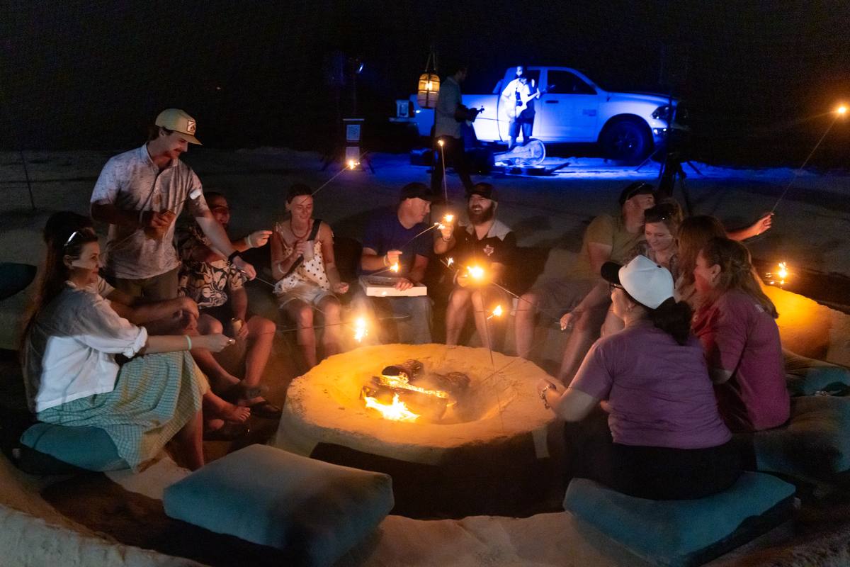Guests gathered around a glowing Twin Ember fire pit at night with sparklers and a live musician performing behind them at Cinnamon Shore.