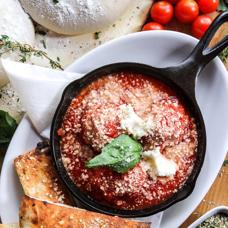 Closeup of Dylan's meatballs marinara in a cast iron skillet with parmesan and basil
