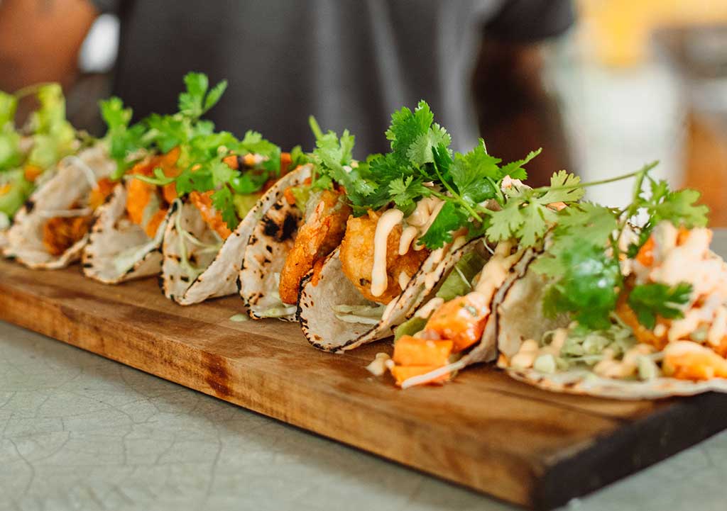 A row of three tacos on a wooden board.