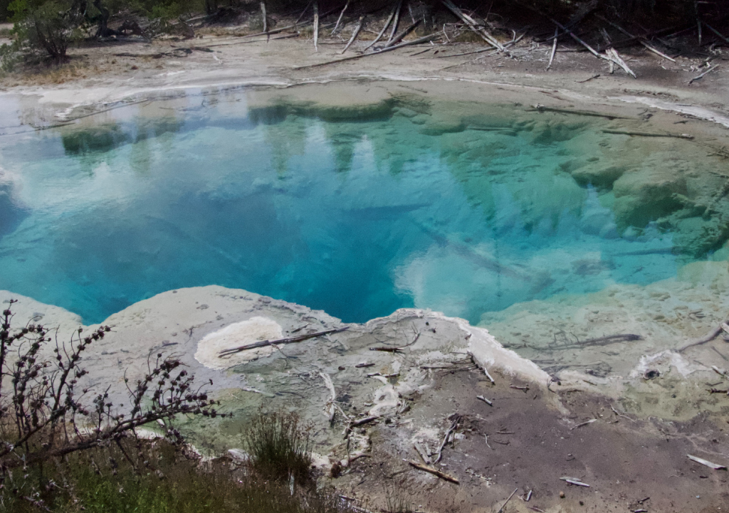 Bright, clear blue water in a large hole surrounded by hard mud at Fifth Water Hot Springs in Utah.