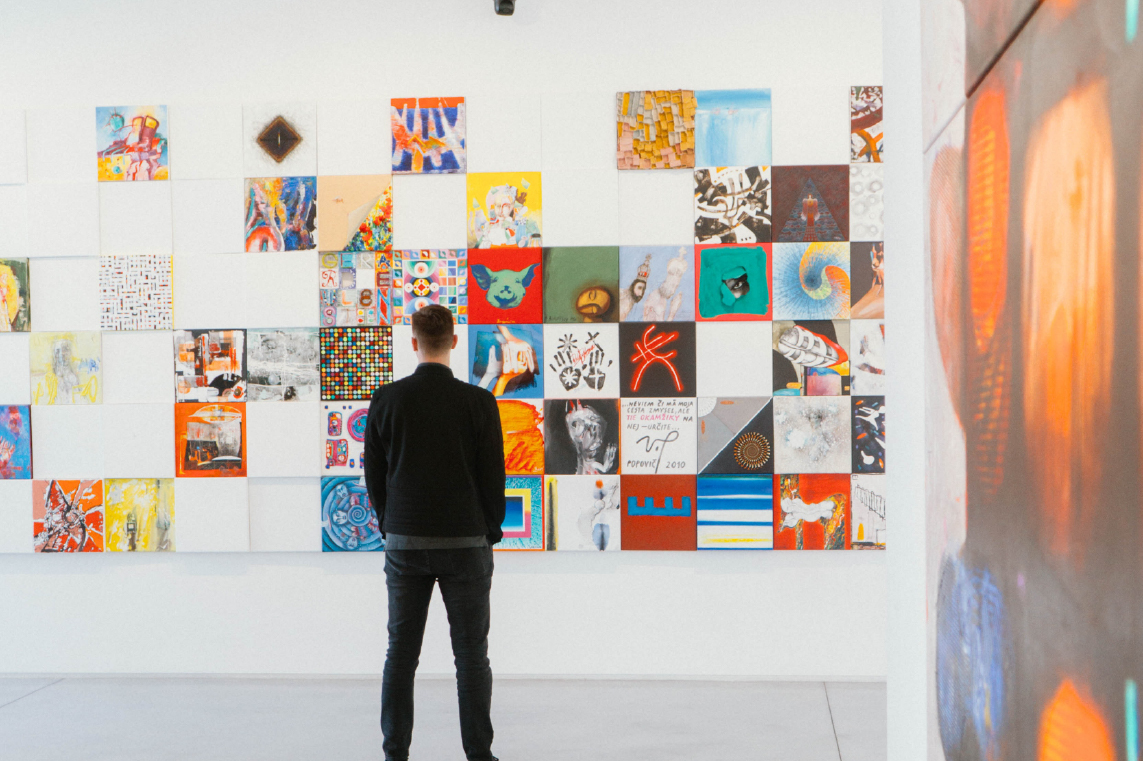 A man standing while viewing a wall of art at a gallery.