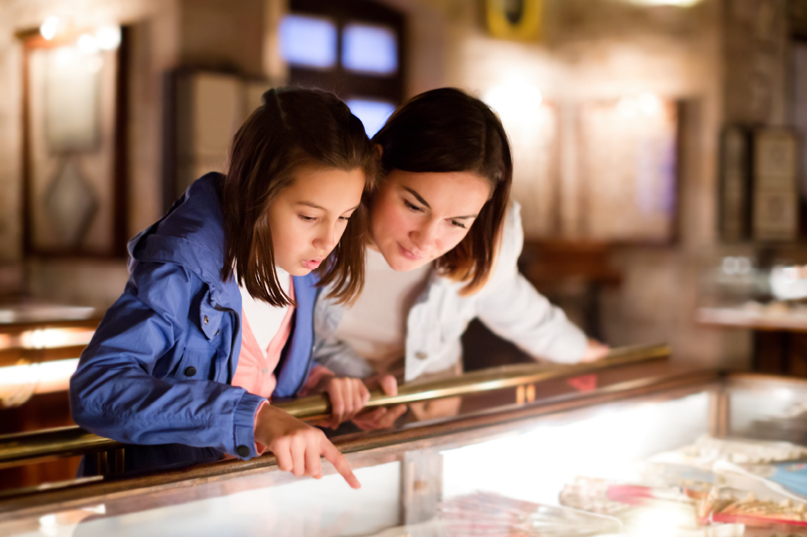 Mother and daughter pointing, looking at museum exhibit in an enclosed case.