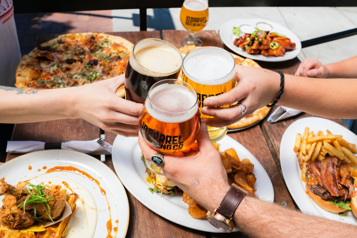 A group of friends clinking their beers together while having food.