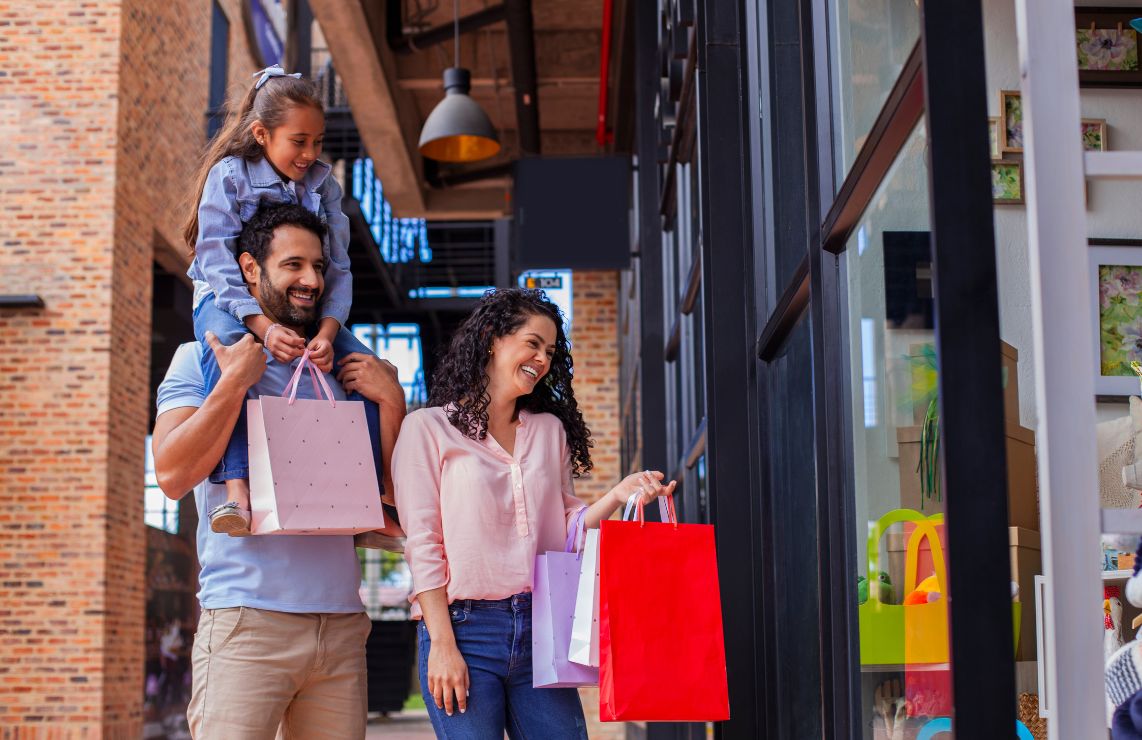 A husband and wife with a little girl hold shopping bags.