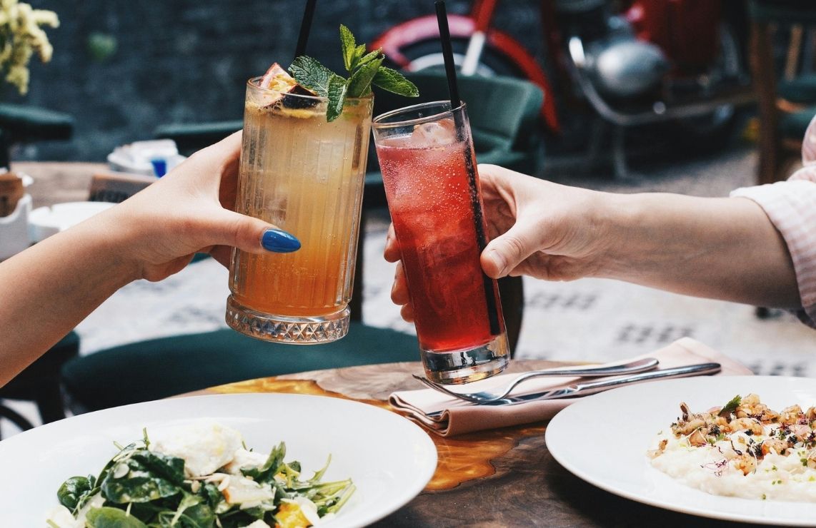 A man and woman clinking glasses with colorful cocktails.