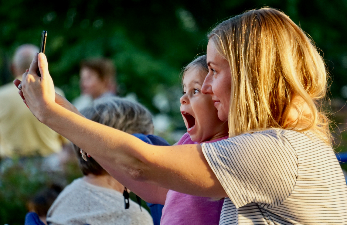 A blonde woman in a striped shirt take a photo of herself and her daughter.