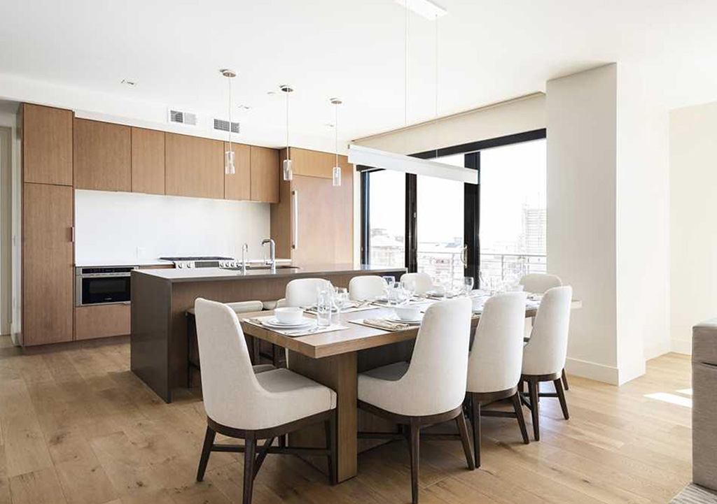 White and light brown modern kitchen with large windows and a dining table that seats eight.