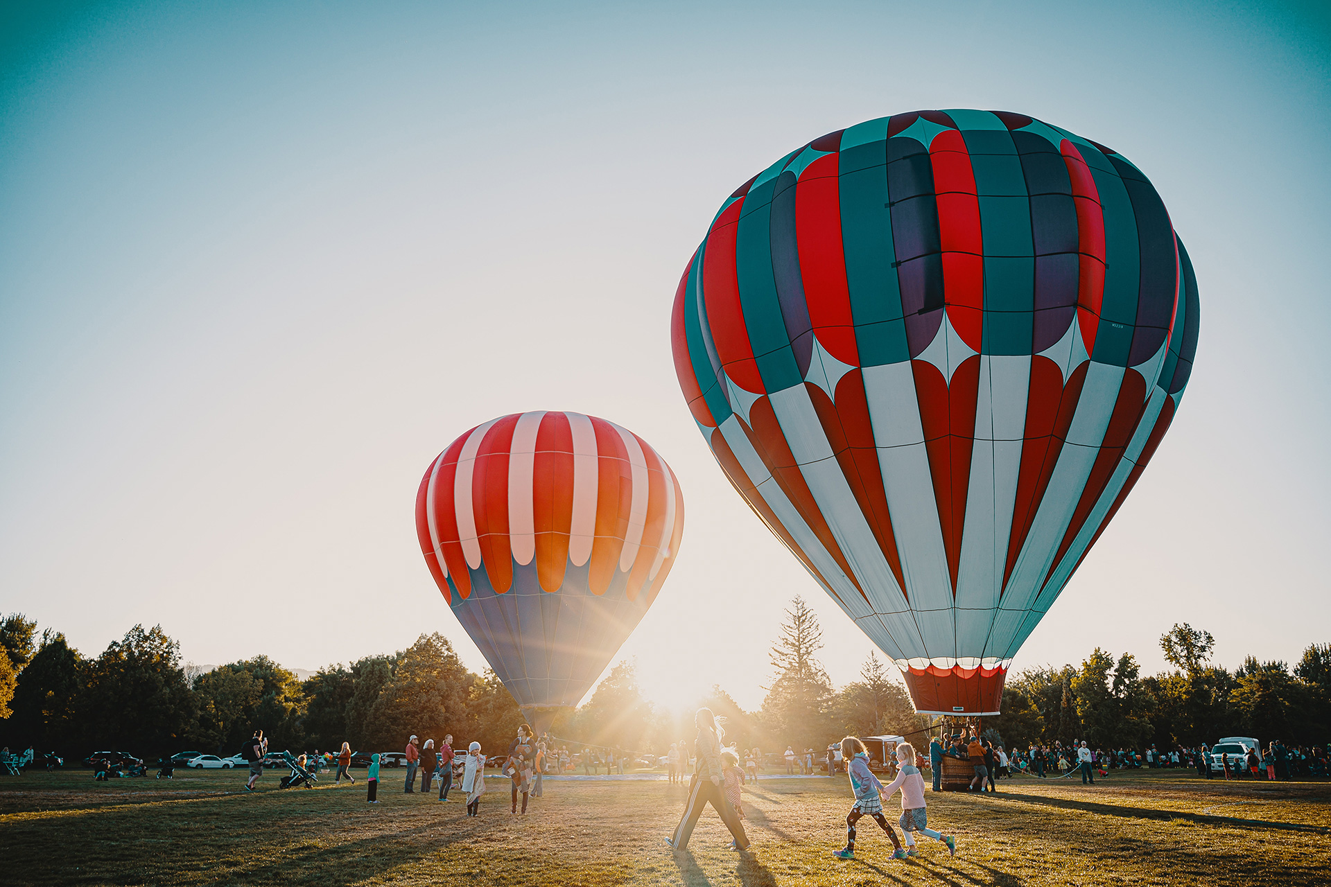 Two hot air balloon surrounded by people in a field about to take off at sunset.