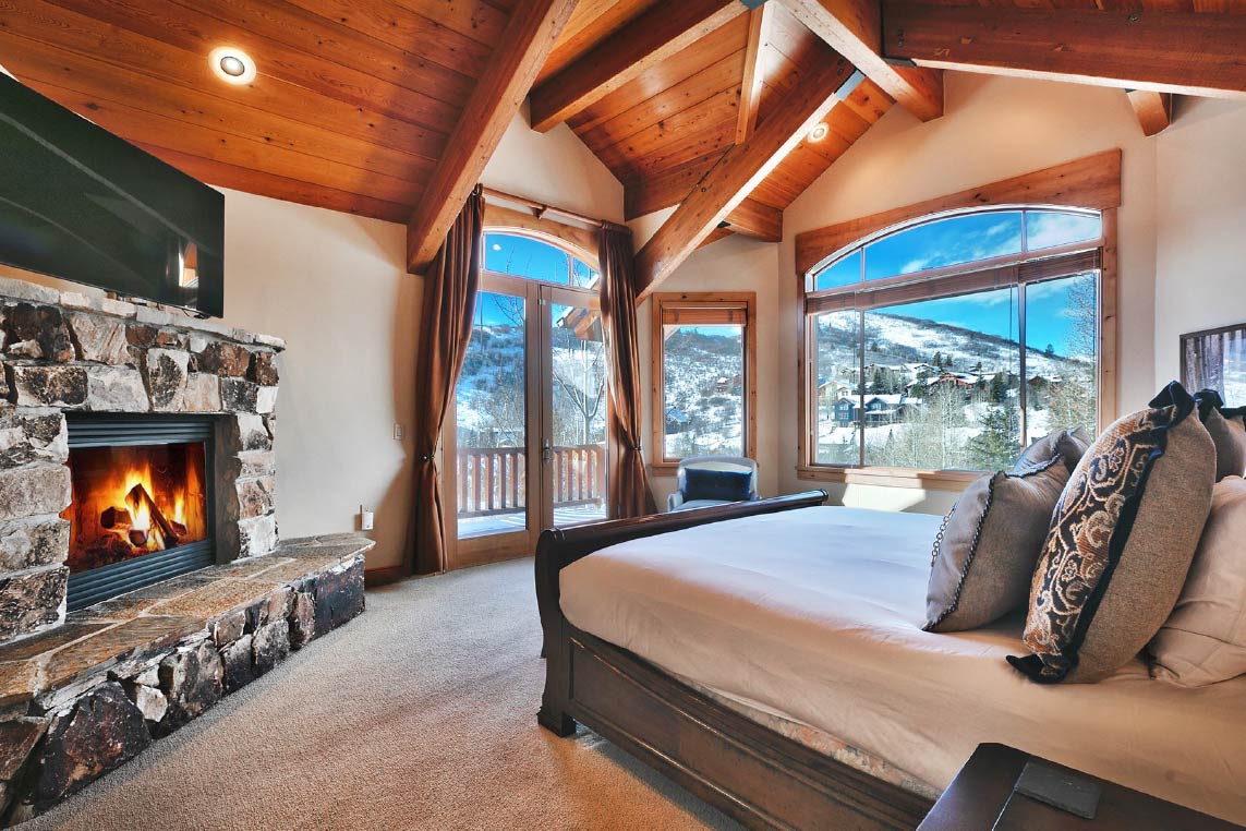 Luxury Park City vacation rental home with fireplace, king size bed, wood ceiling beams, private patio, and views of Park City's mountains in winter.