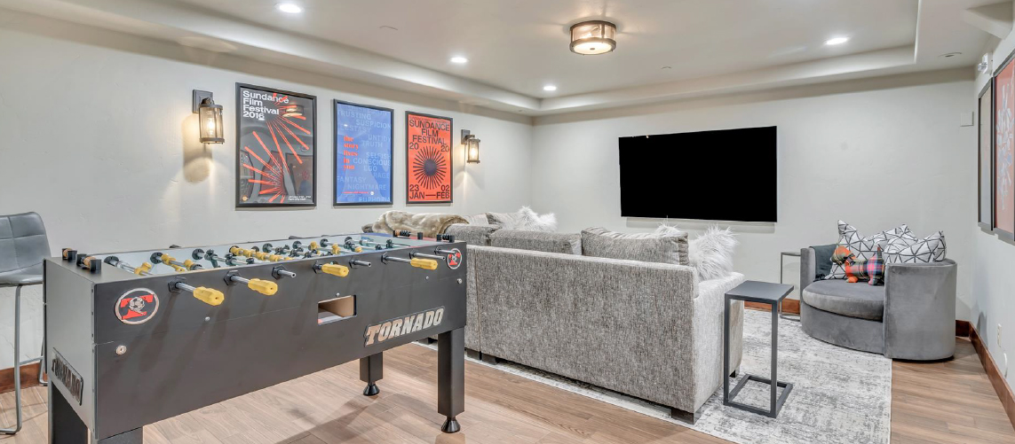 The basement of a private rental home includes a game room with large screen TV and foosball table.