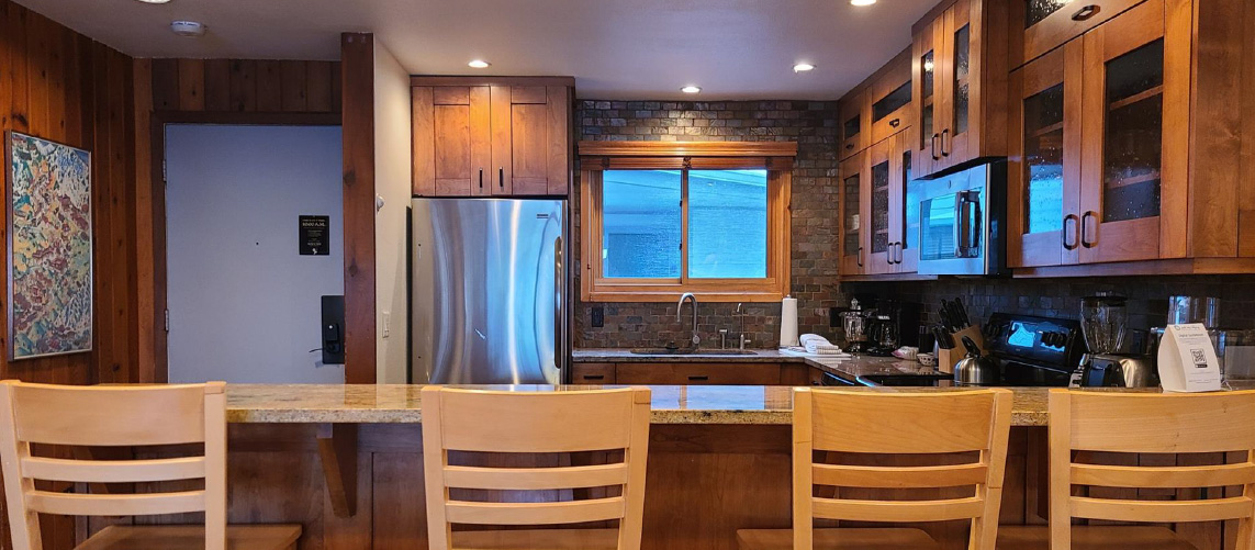 Condo kitchen with seating for four at the countertop, stainless steel appliances, and cherry wood cupboards.