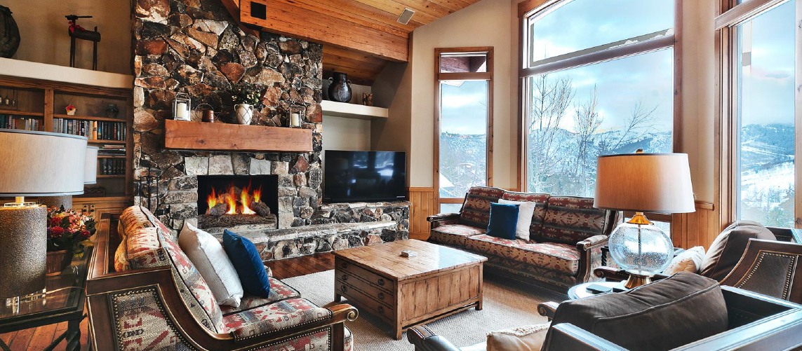 Rustic lodge-style rental home with views of Park City mountains and includes large wood burning fireplace and cozy couches.