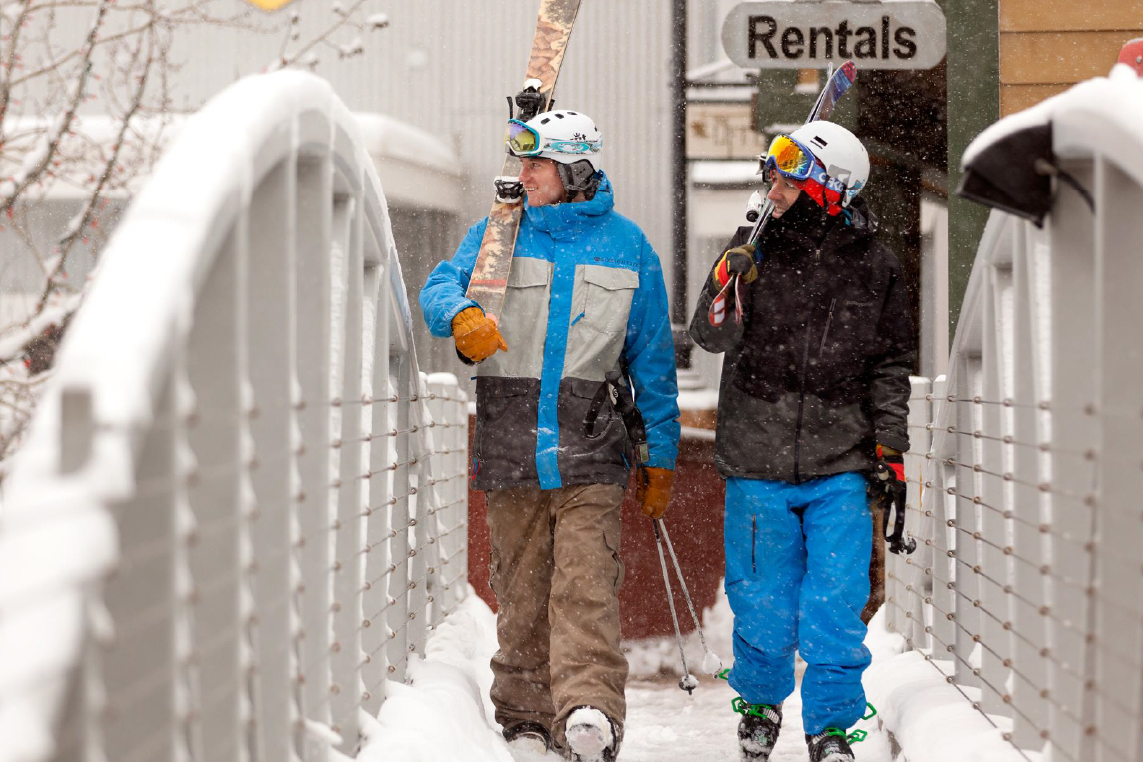Two men in brightly colored ski gear walk across the snow during a Park City winter vacation.
