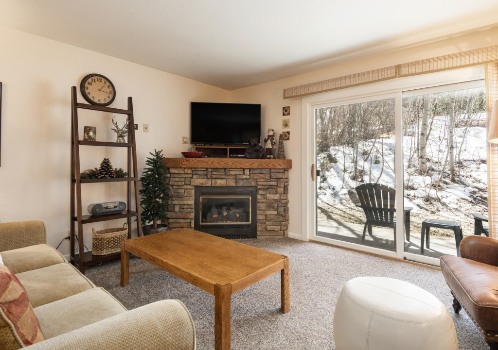 Snow Flower condo living room featuring stone fireplace and a snowy view outside sliding doors.