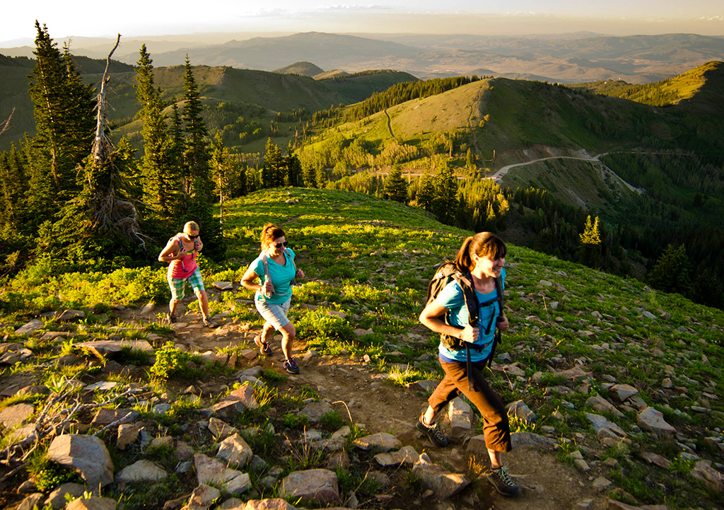 Three women hiking on sunny, green mountain in Park City, Utah.