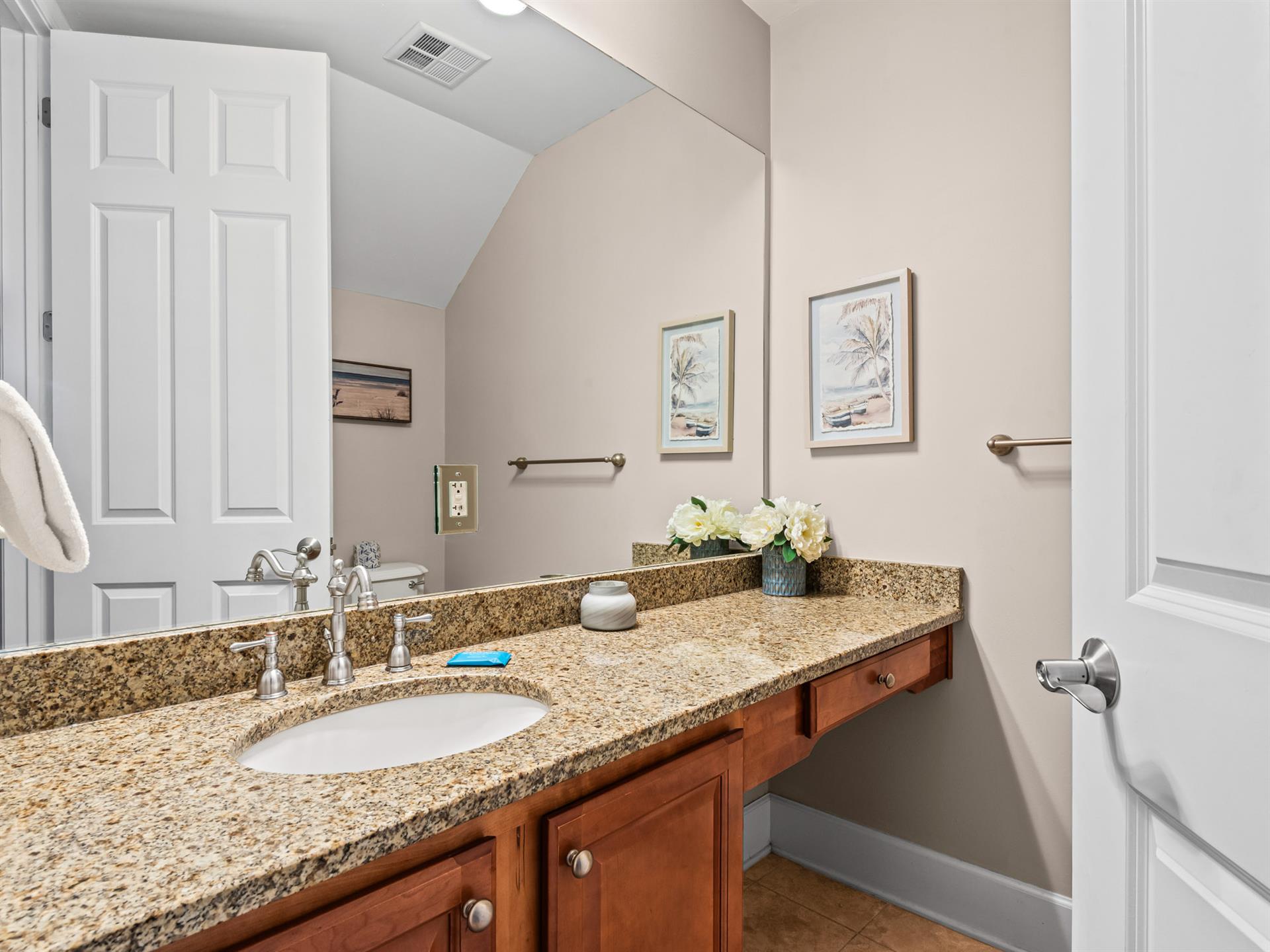 Half bathroom featuring granite countertops, warm wood cabinetry, and thoughtful coastal artwork that creates a serene atmosphere for your daily routine.