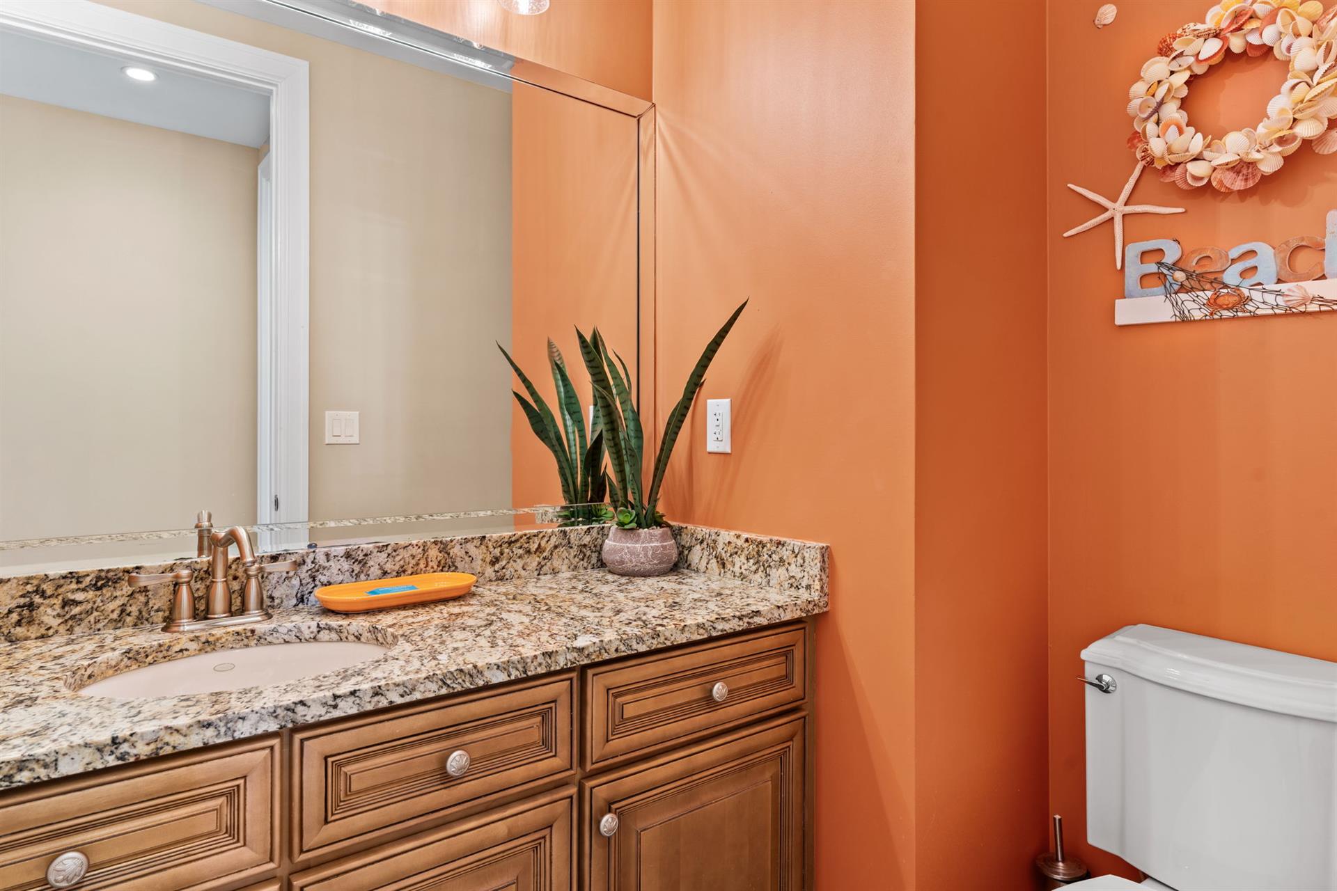 Refresh in your vibrant coral hallway half bathroom featuring granite countertops, coastal touches, and thoughtful amenities for your comfort.