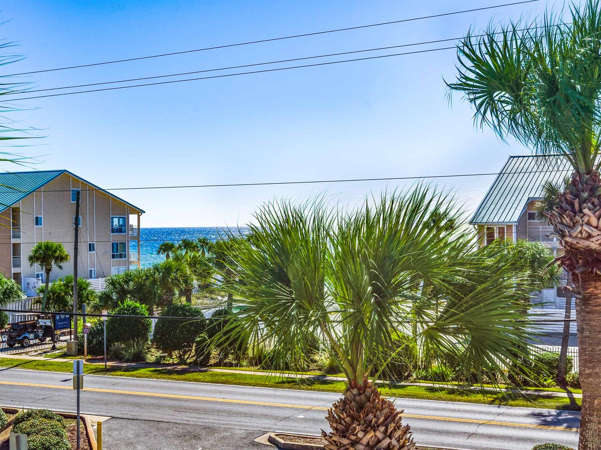 Coastal property with tropical palm trees and nearby beachfront buildings under clear blue skies.