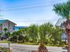 Coastal property with tropical palm trees and nearby beachfront buildings under clear blue skies.