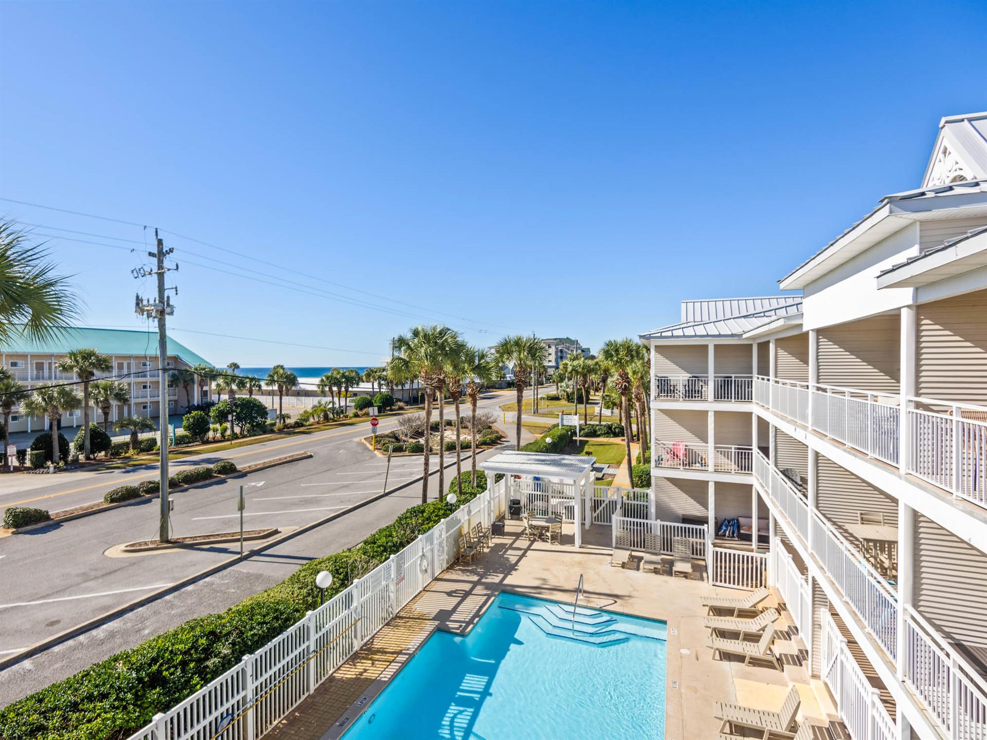 Elevated view showcasing the propertys swimming pool and balconies, with palmlined streets leading toward the nearby beach.