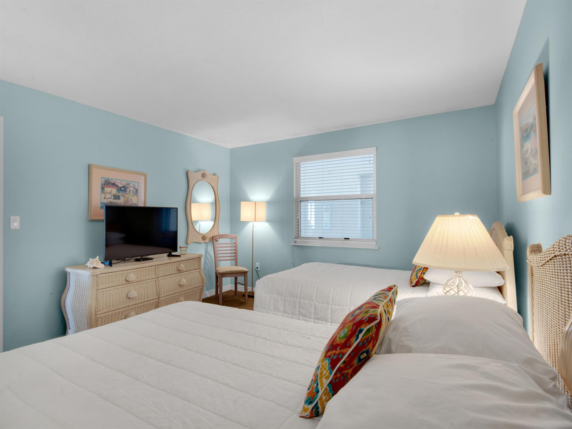 Rest peacefully in this serene double bedroom with soft coastal colors, comfortable beds, and charming wicker furnishings.
