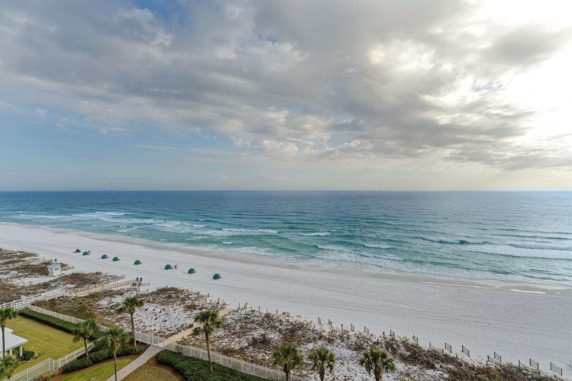 Pristine white sand beach stretches along emerald waters with beach umbrellas dotting the shoreline.