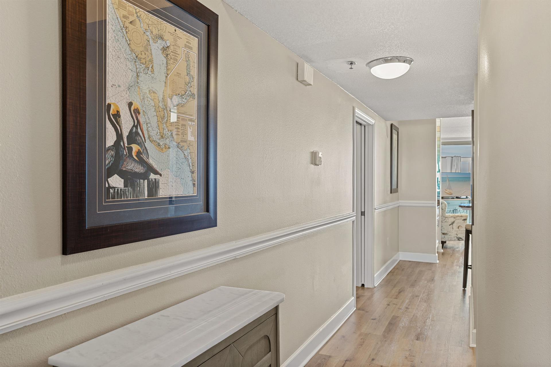 Inviting hallway with coastalthemed artwork and warm hardwood floors leading to your bright oceanfront spaces.