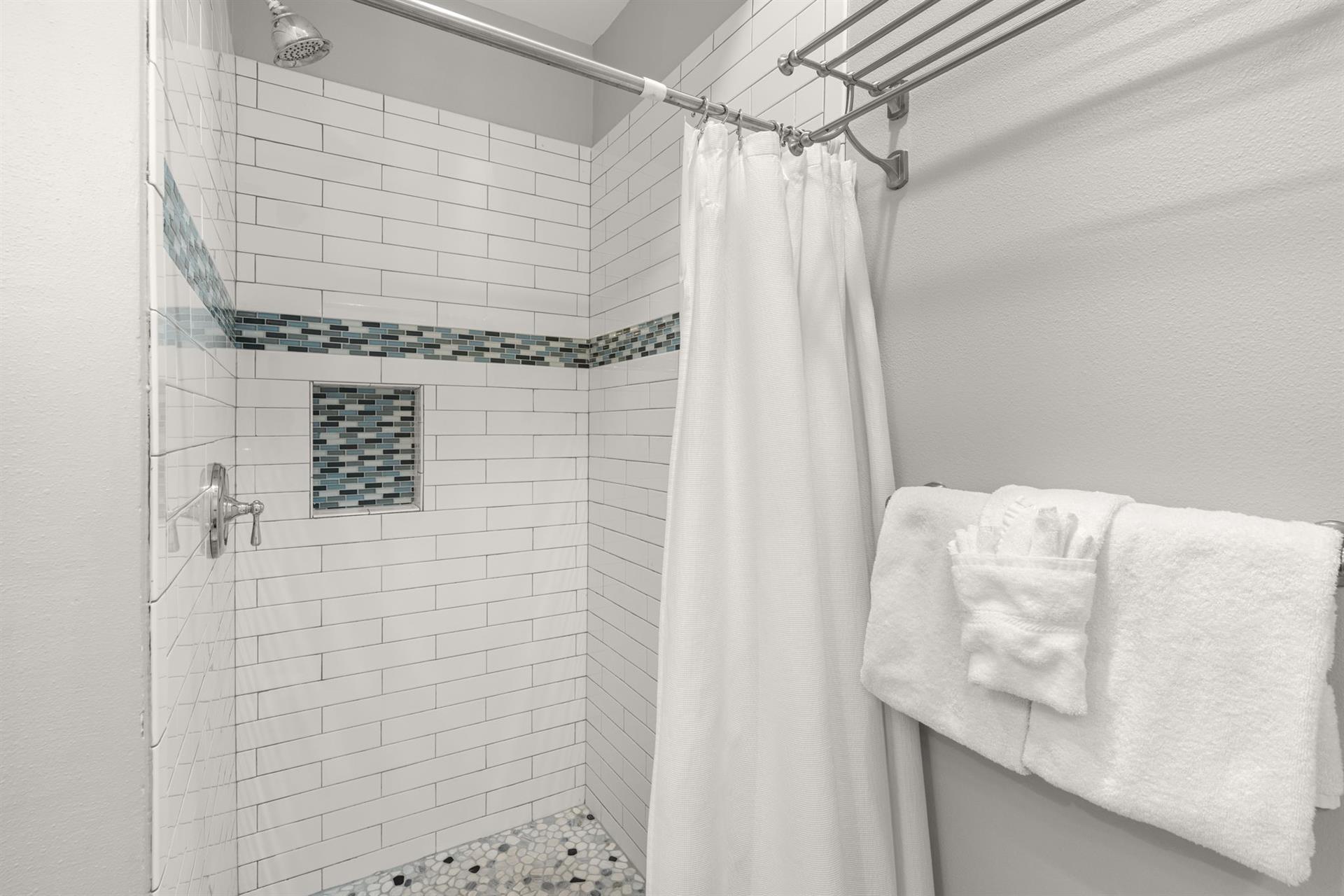 Step into the pristine tiled shower featuring elegant white subway tiles and blue mosaic accents with fluffy towels awaiting.