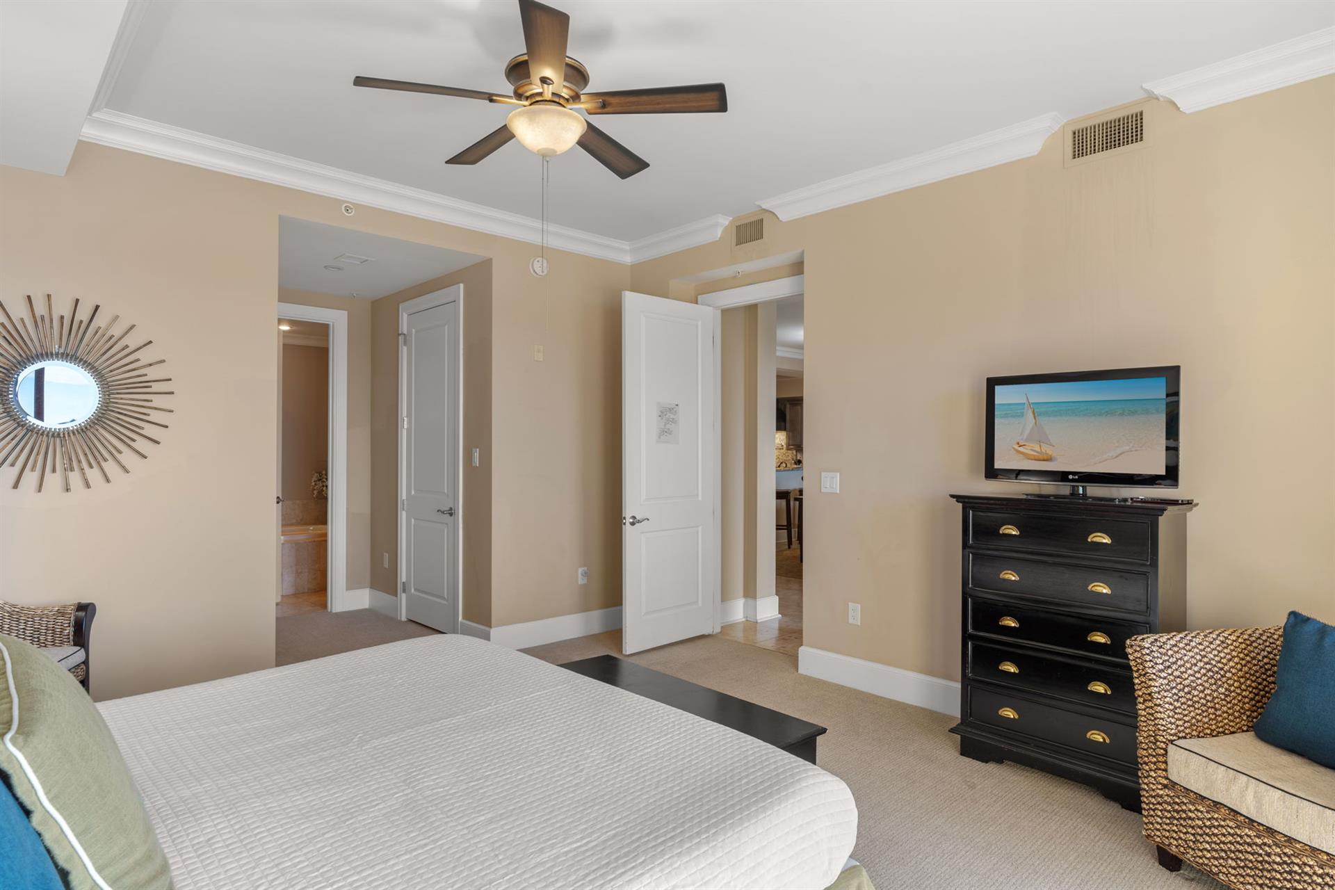 Relax in your elegantly appointed bedroom featuring a ceiling fan, flatscreen TV, and coastal artwork that sets a peaceful vacation mood.