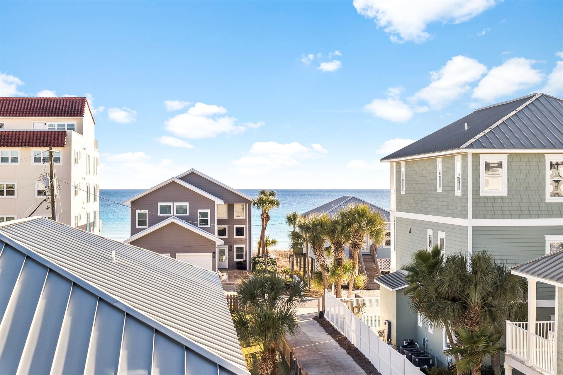 Coastal neighborhood with beach houses and palm trees leading to pristine ocean waters and sandy shores.
