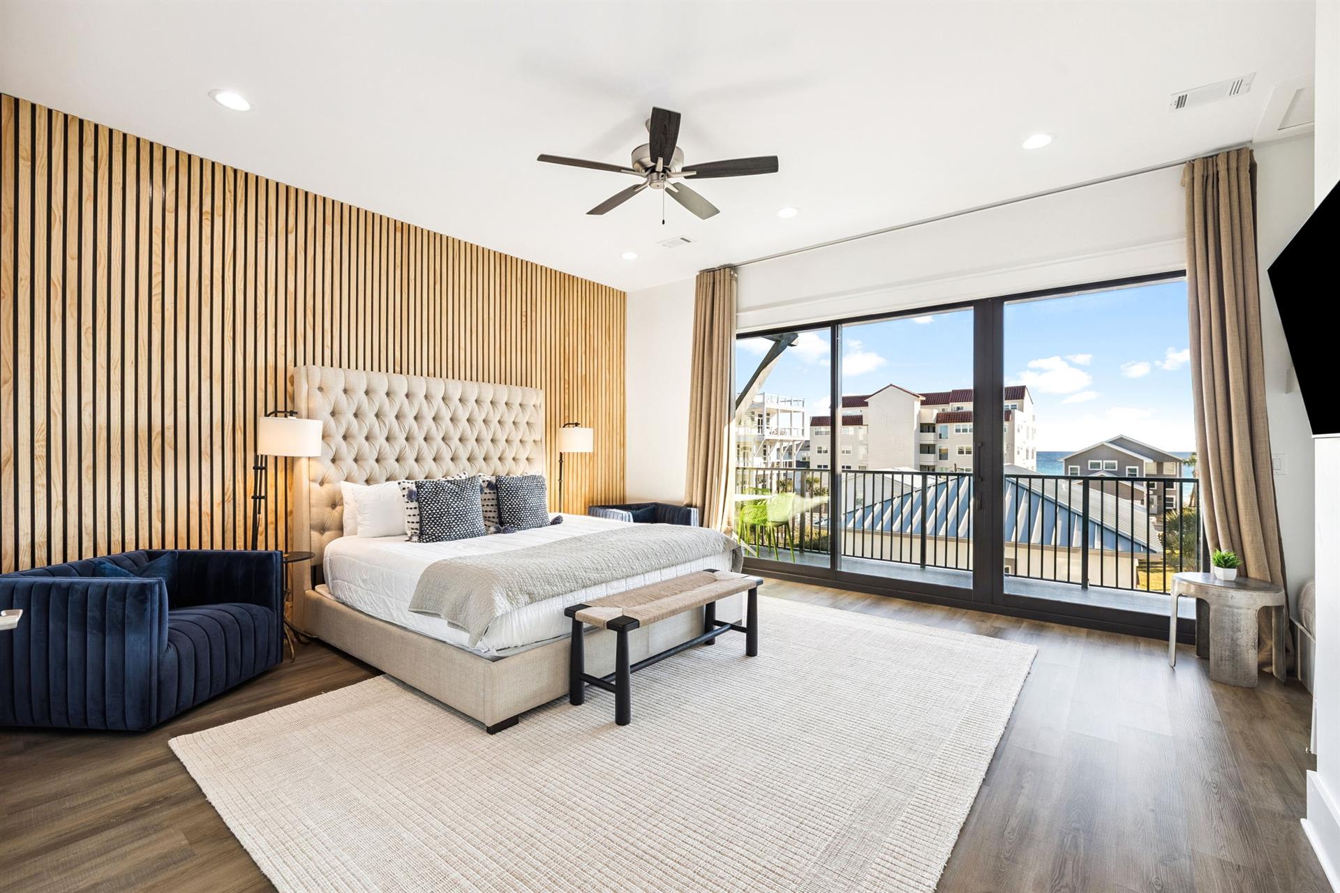 Unwind in the elegant primary suite featuring a luxurious tufted headboard, modern wood slat accent wall, and private balcony access.