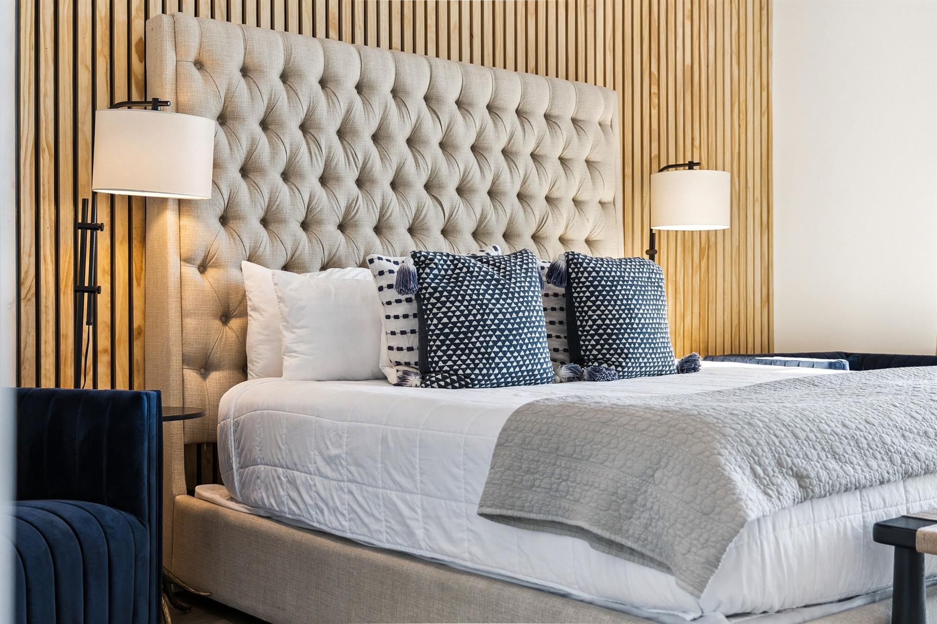 Sink into luxury with your plush tufted headboard and crisp linens, perfectly complemented by warm wood paneling and elegant bedside lighting.