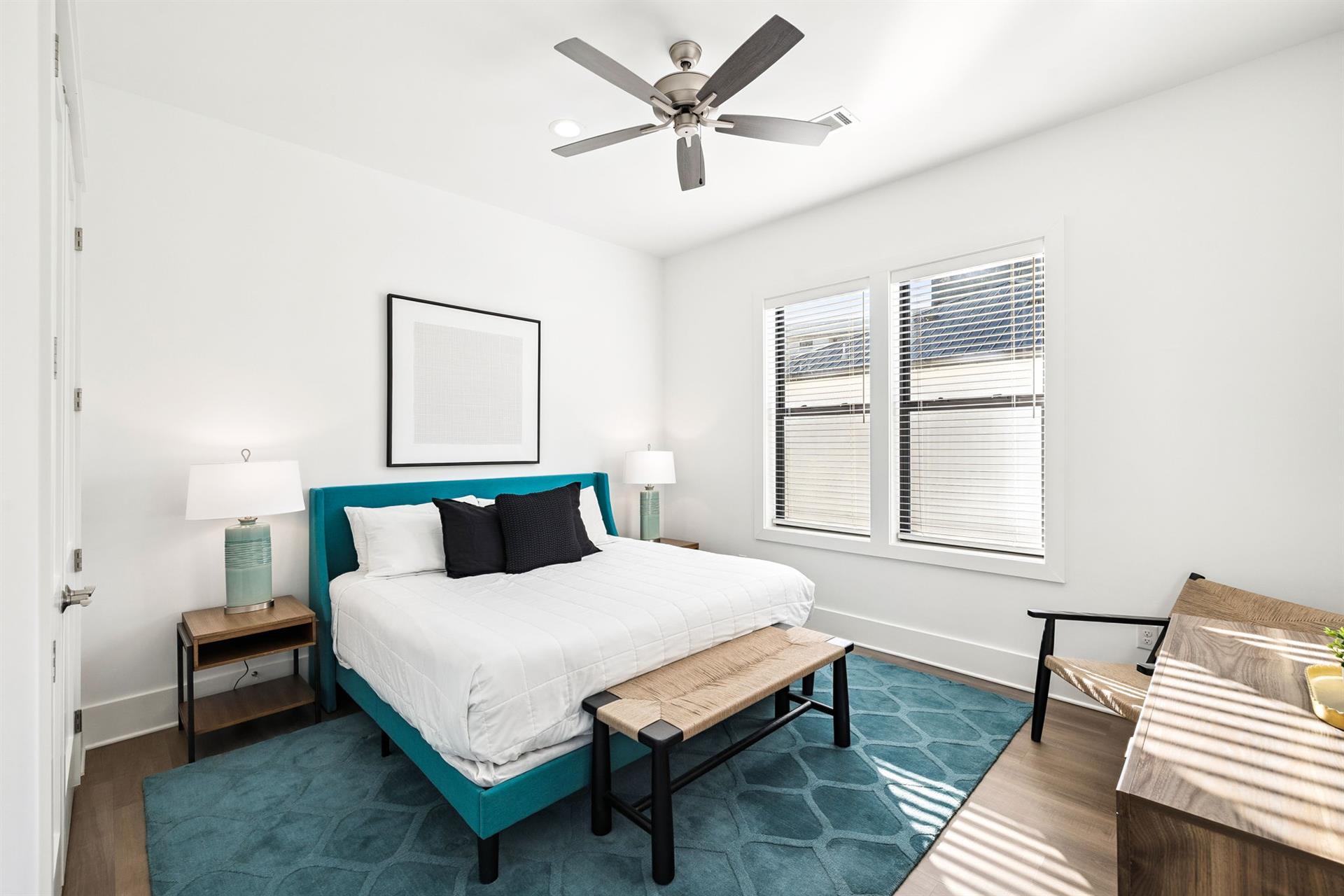 Rest peacefully in your bright bedroom featuring a plush teal bed, modern ceiling fan, and warm natural light streaming through oversized windows.