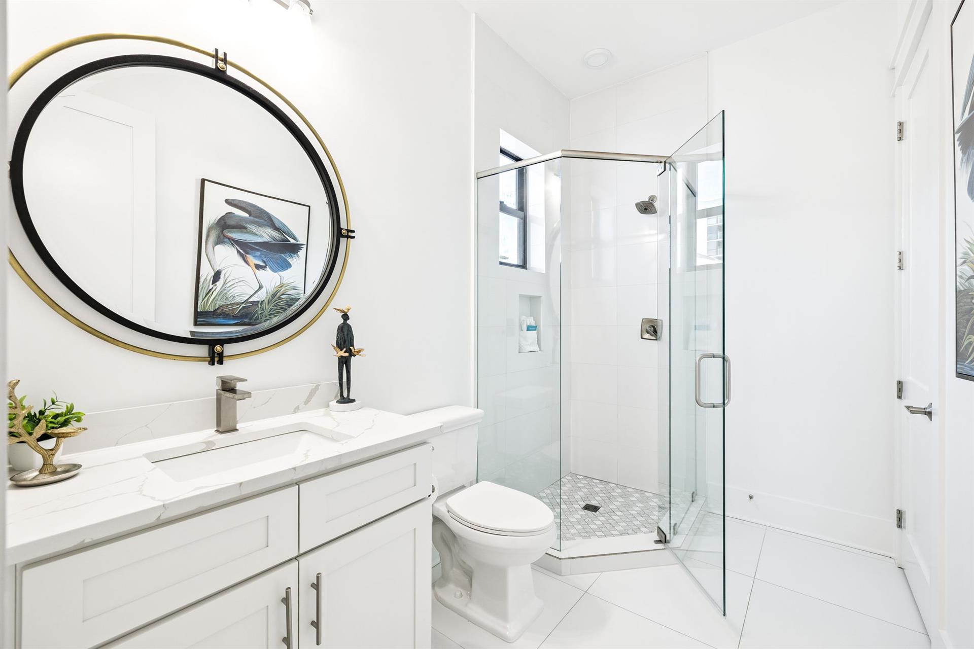 Refresh in your pristine white bathroom featuring a sleek glass shower, elegant round mirror, and marble countertops—your perfect morning retreat.