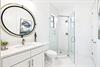 Refresh in your pristine white bathroom featuring a sleek glass shower, elegant round mirror, and marble countertops—your perfect morning retreat.