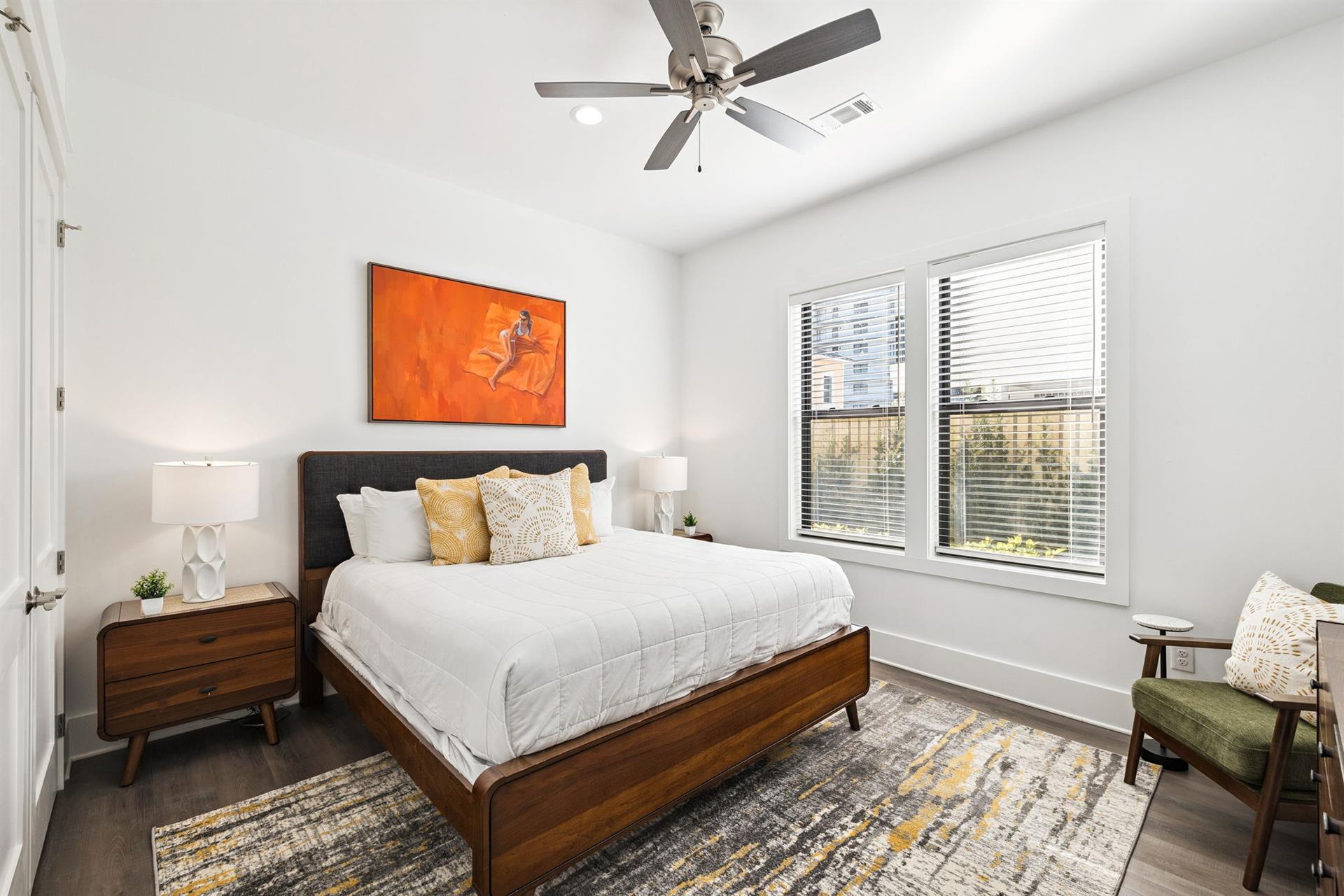 Your serene bedroom sanctuary features a plush bed beneath gentle ceiling fan breezes and natural light streaming through large windows.