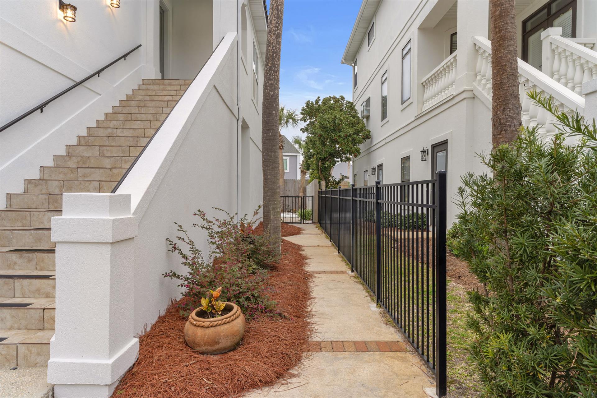 Elegant white building entrance featuring charming landscaping with mulched garden beds and mature palm trees in a peaceful residential setting.