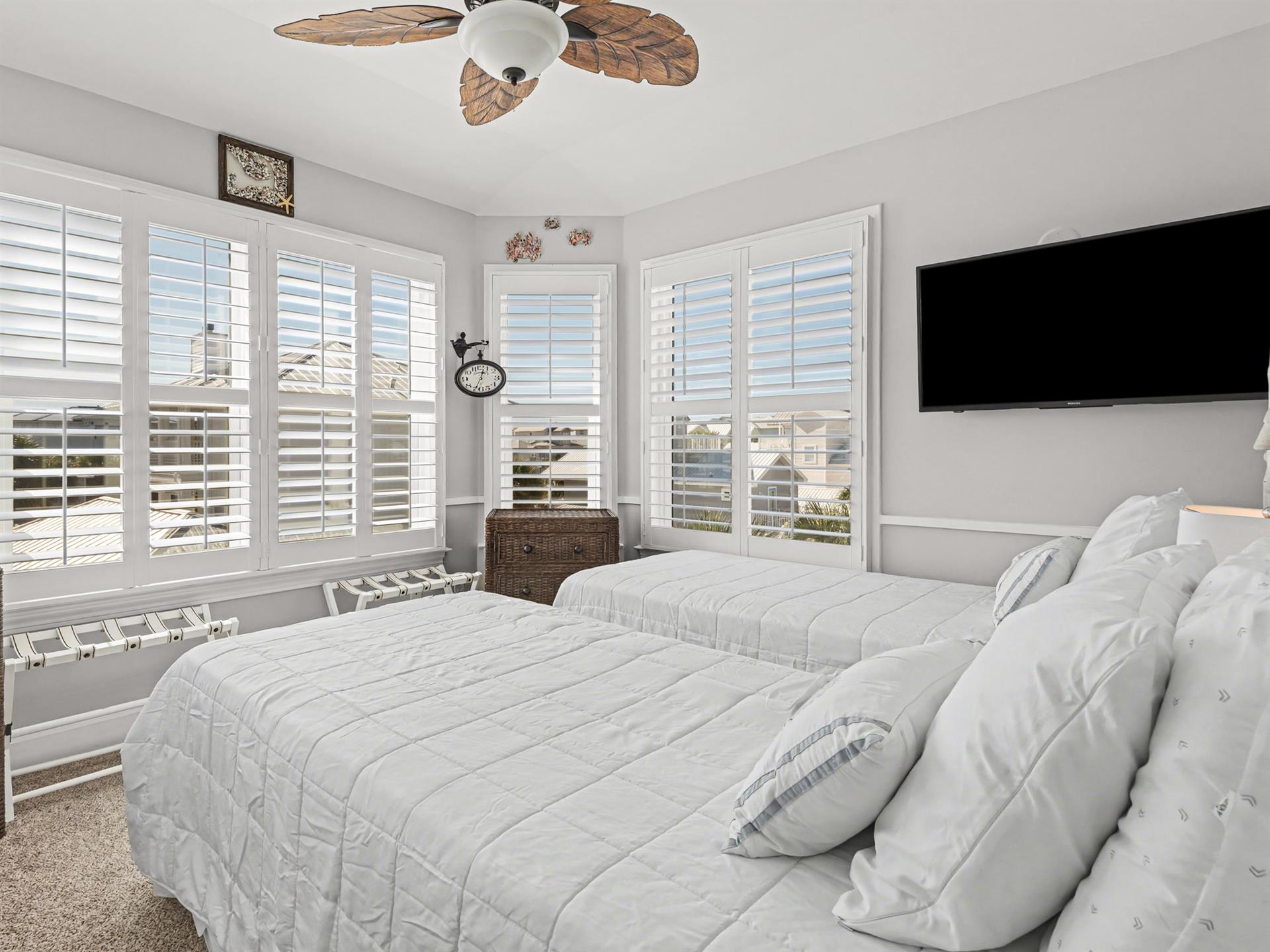 Wake to gentle ocean breezes in your bright bedroom with twin beds, ceiling fan, and large windows framing coastal views.