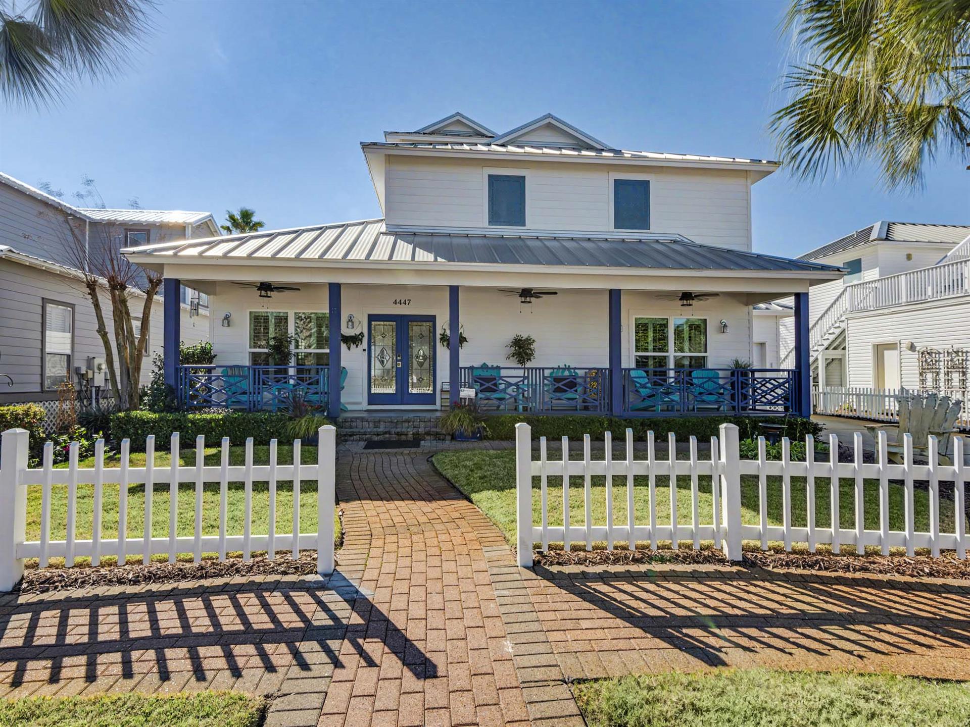 Charming coastal home with turquoise accents and welcoming front porch surrounded by tropical palms and picket fence.