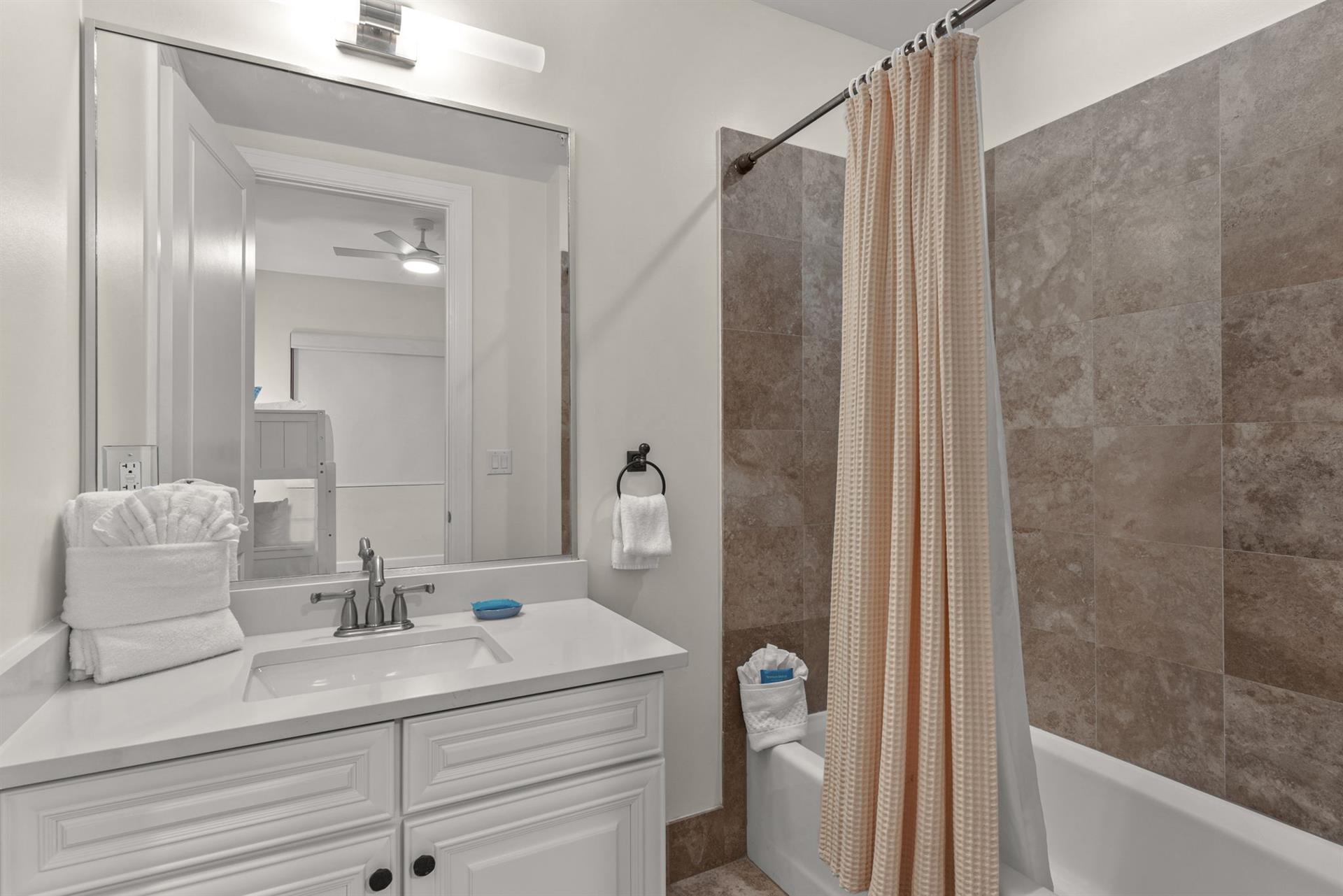 Unwind in your elegant bathroom featuring tile walls, crisp white vanity, and plush towels awaiting your arrival.