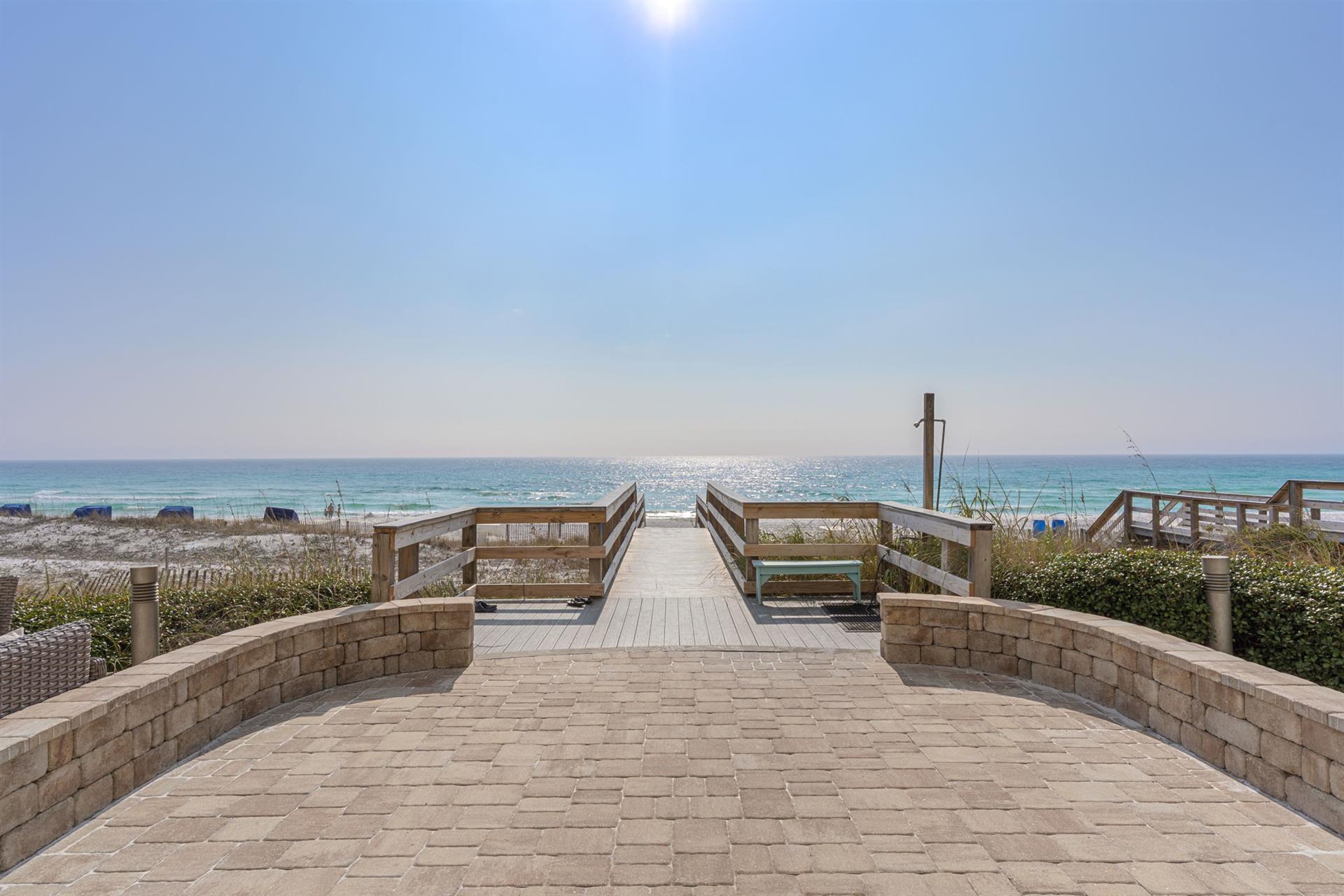 Stonepaved pathway leads through dunes to pristine white sand beach and emerald waters on this stunning Gulf Coast stretch.