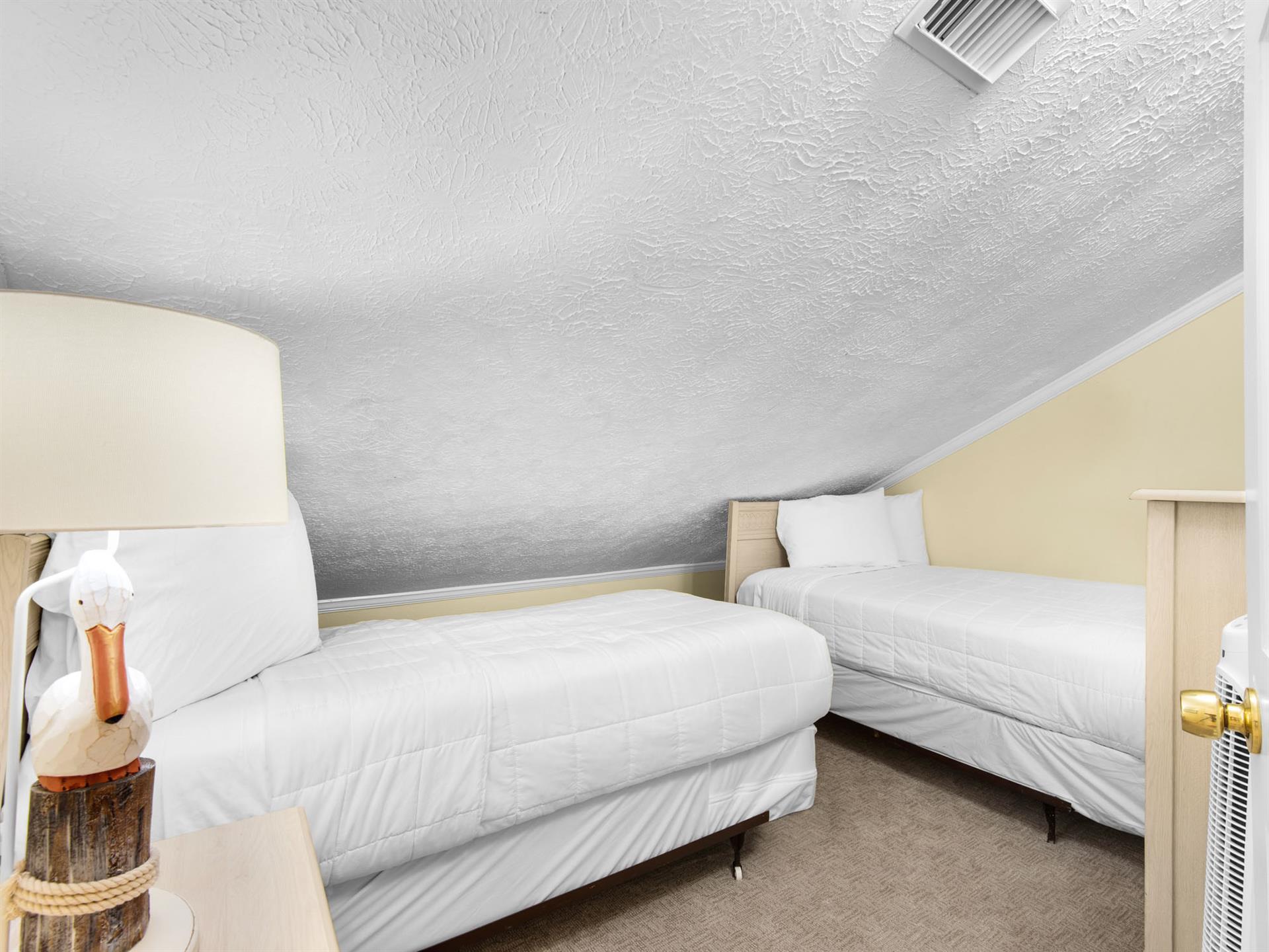 Cozy bedroom features 2 twin beds under slanted ceilings, creating an intimate retreat perfect for restful nights.